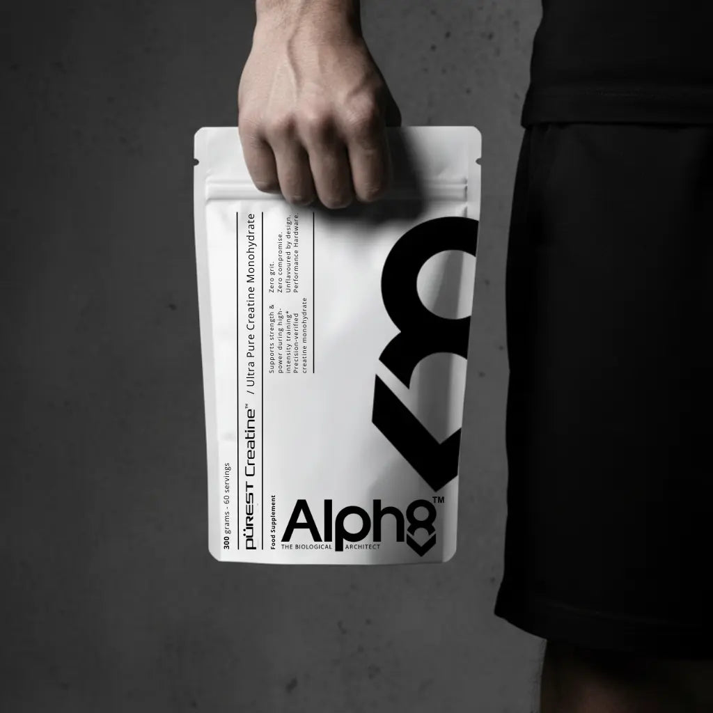 Person holding a white supplement package with 'Alph8' branding against a dark background